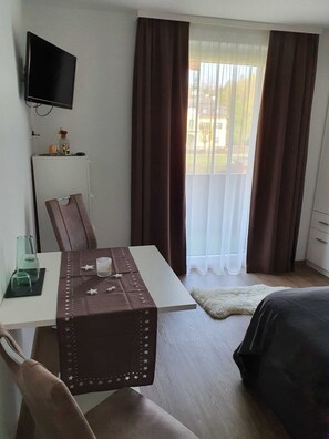 A hotel room with a bed, a desk with a chair, a television mounted on the wall, and a window with curtains. - Apartment 3 - Apartment house Roland (Strobl)