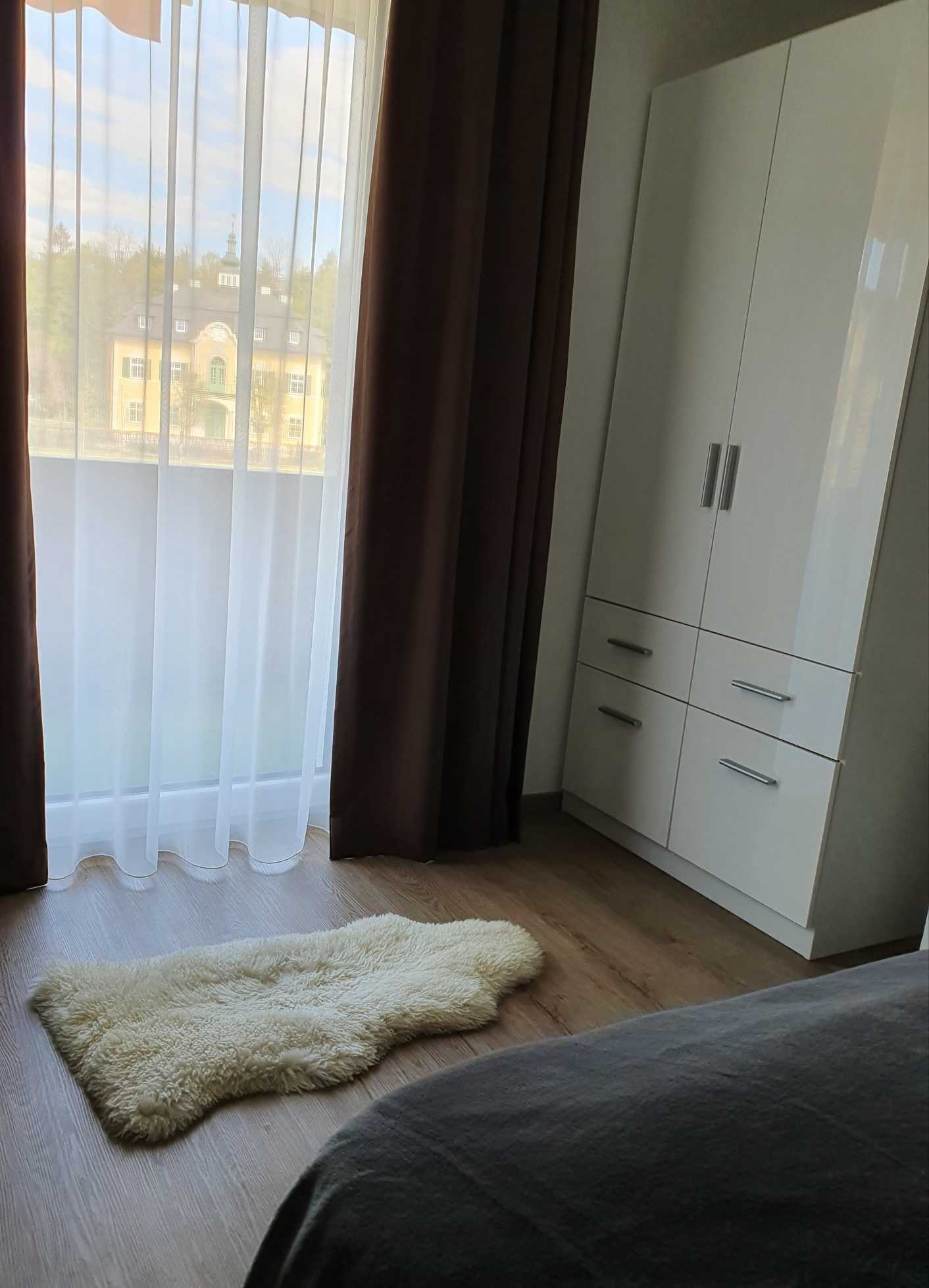 Une chambre dotée d’une grande armoire, d’un tapis moelleux et offrant une vue sur un immeuble à travers des rideaux transparents.