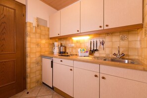 A compact kitchen with wooden cabinets, a built-in dishwasher, and a countertop with a coffee maker, kettle, and utensils. - Apartment 3 - Apartment house Roland (Strobl)