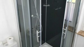 Een douchecabine met glazen wanden, een wit toilet en een rol toiletpapier ernaast.