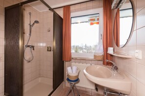 A bathroom with a shower, a sink, a window with curtains, and a mirror. - Apartment 3 - Apartment house Roland (Strobl)