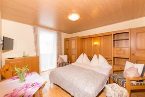 A bedroom with a bed, a wooden dresser, a chair, a table with a vase, and a television on the wall. - Apartment 3 - Apartment house Roland (Strobl)