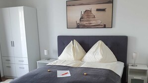 Een slaapkamer met een bed, een witte kledingkast, nachtkastjes en een aan de muur bevestigd schilderij.