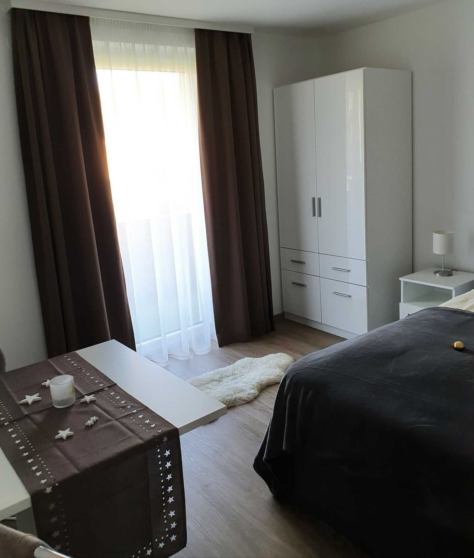 Habitación de hotel con cama, armario, mesita de noche con lámpara y una pequeña mesa con una vela y adornos de estrella.