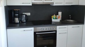 Een kleine keuken met witte kastjes, een zwart aanrecht, een koffiezetapparaat, een waterkoker en een spoelbak.