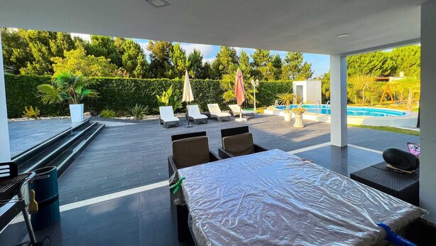 Un patio moderno al aire libre con piscina, sillones de descanso y una zona de estar cubierta.