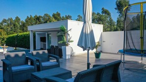 Un patio con mobiliario de mimbre, un edificio blanco y un trampolín.