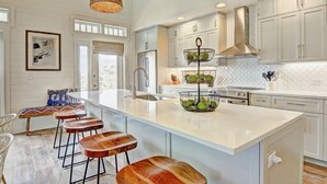 Una cocina moderna con armarios blancos, una isla grande con taburetes y una lámpara colgante.