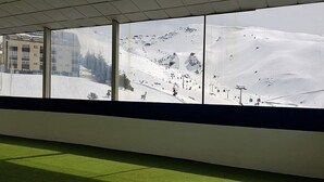 Uitzicht op een skipiste door grote ramen, met een gebouw op de achtergrond.