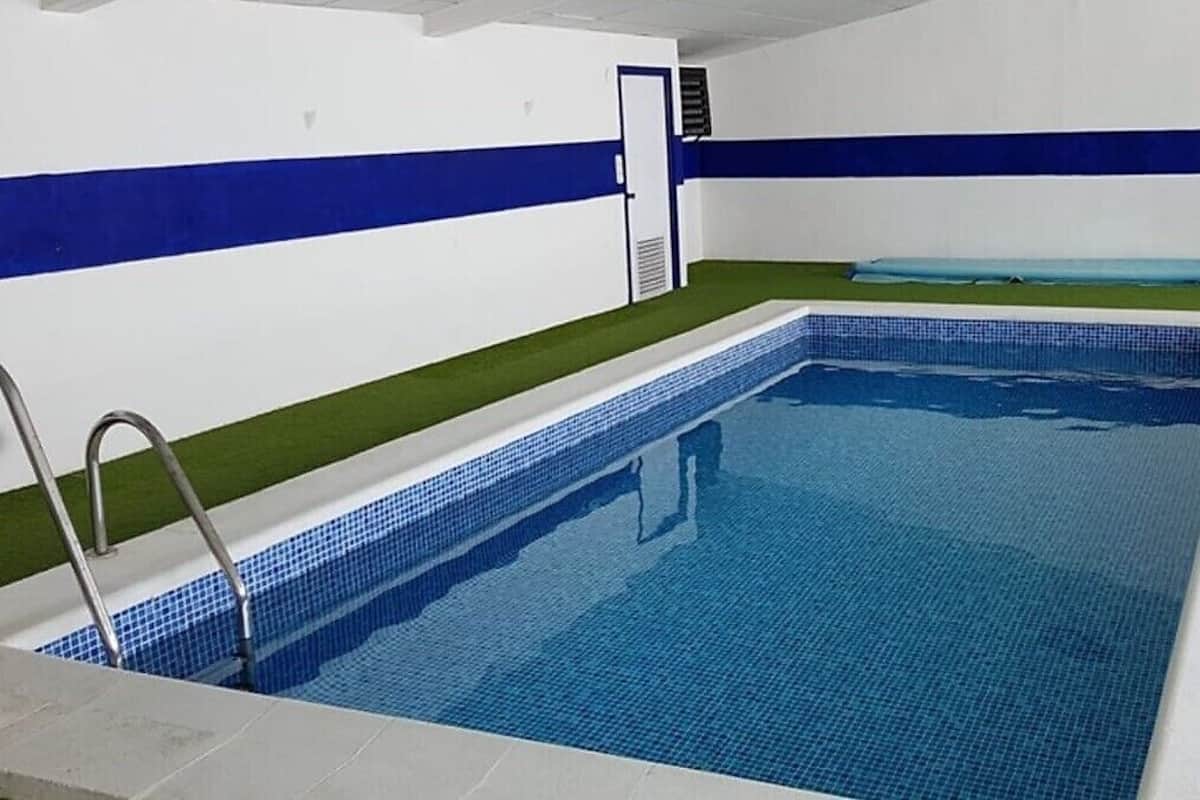 An indoor swimming pool with a tiled floor, a ladder, and a door.
