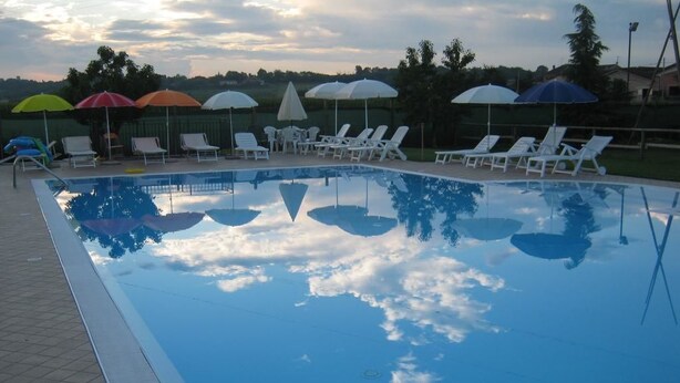 Ein rechteckiger Pool mit Fliesen umgeben, umrahmt von weißen Liegestühlen und Sonnenschirmen.