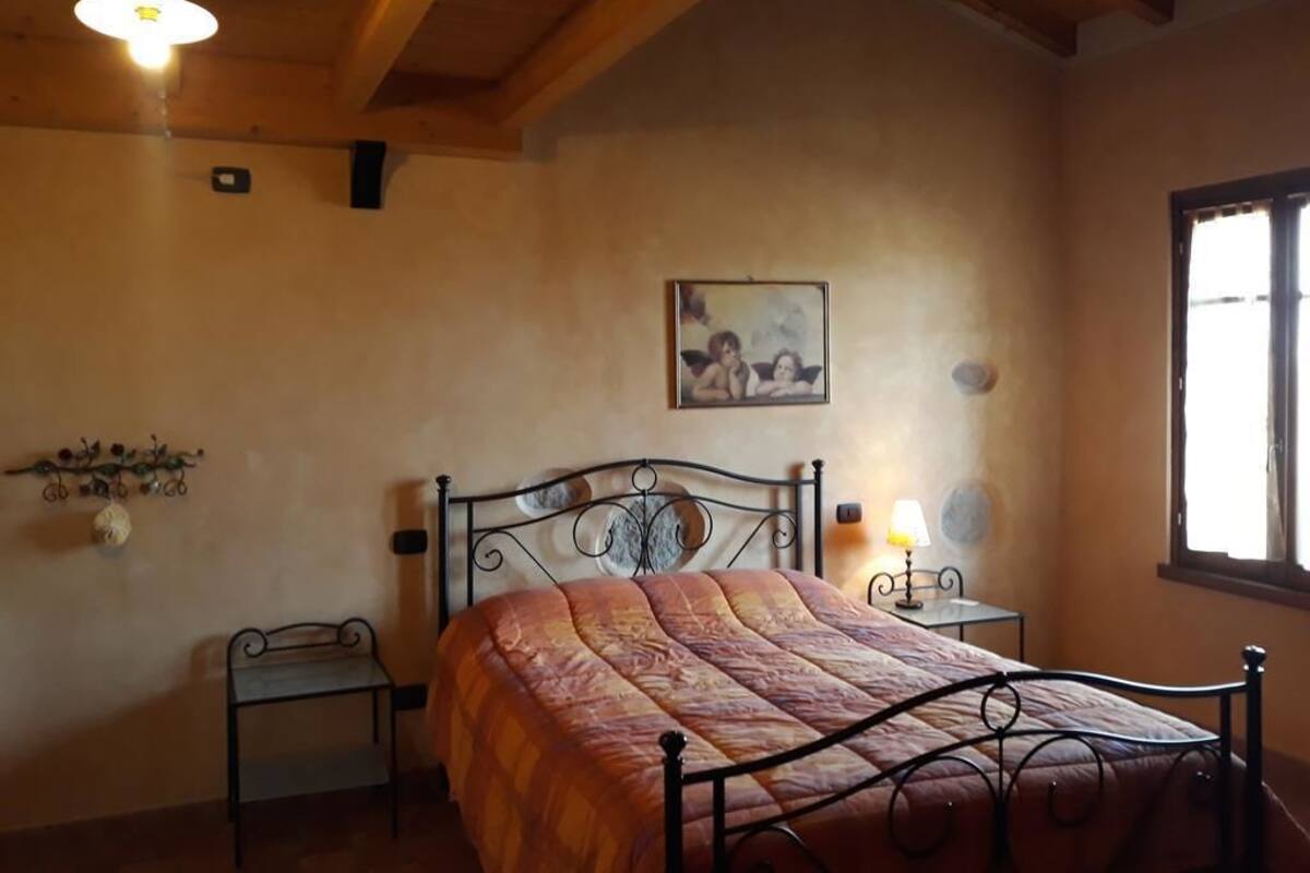 Een slaapkamer met een bed, nachtkastje, wandlamp, klein tafeltje en een raam.