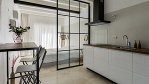 Une cuisine moderne avec un plan de travail en bois, un évier et une hotte noire. On y trouve un coin repas avec une table et des chaises, ainsi qu’une grande fenêtre avec des rideaux.