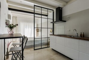 Une cuisine moderne avec un plan de travail en bois, un évier et une hotte noire. On y trouve un coin repas avec une table et des chaises, ainsi qu’une grande fenêtre avec des rideaux.