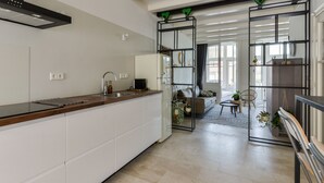 Une cuisine moderne avec un plan de travail en bois et des meubles blancs, qui donne sur un espace de vie comprenant un canapé, des fauteuils et des plantes en pot.