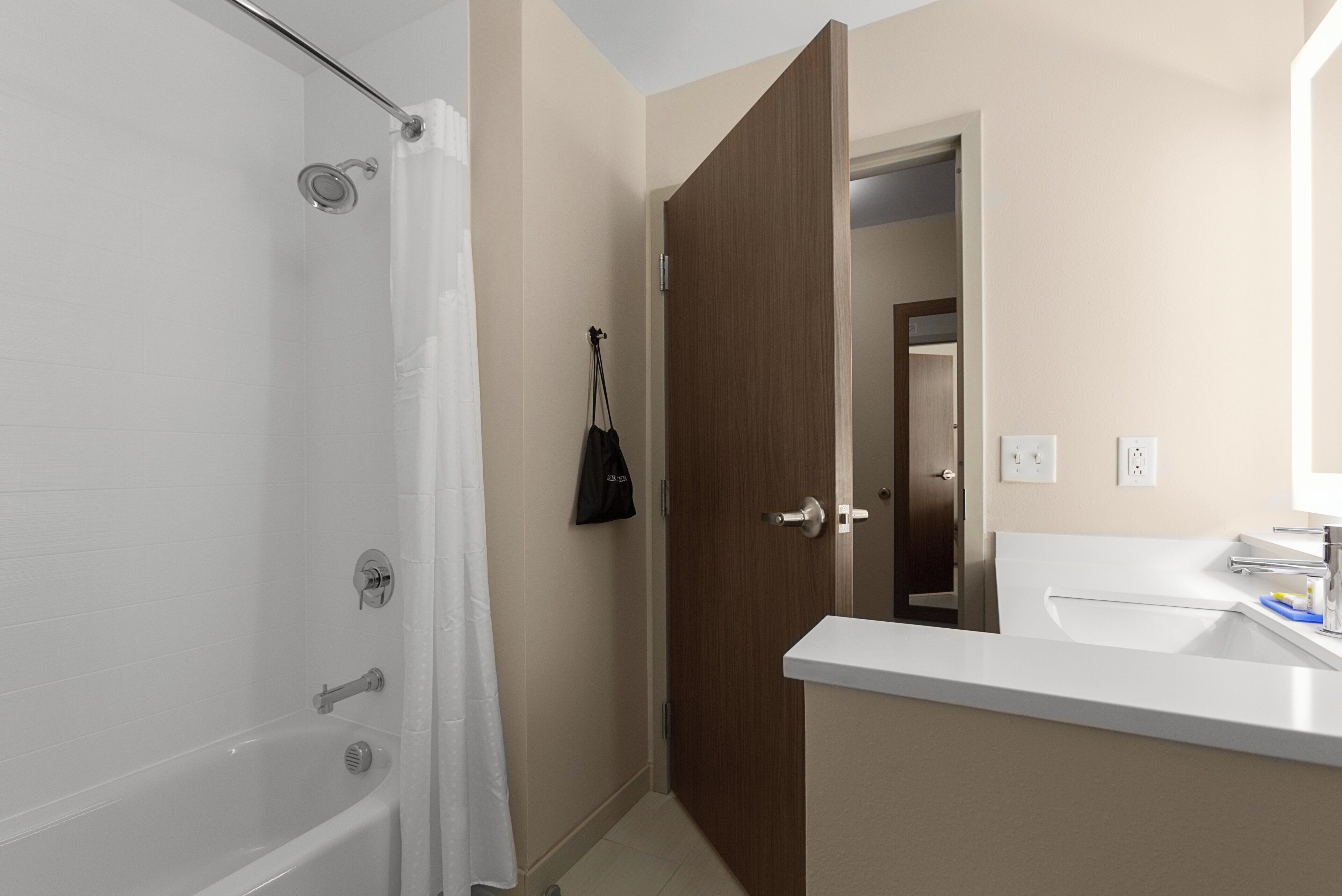 A bathroom with a bathtub, a shower, a sink, and a door leading to another room.
