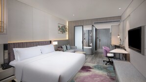 Une chambre d’hôtel moderne, dotée d’un grand lit, d’un bureau, d’une chaise, d’une télévision et d’une salle de bain visible à travers une porte ouverte.