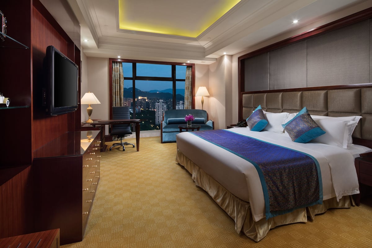 Habitación de hotel con una cama grande, un escritorio, una silla, un televisor y vistas a la ciudad.