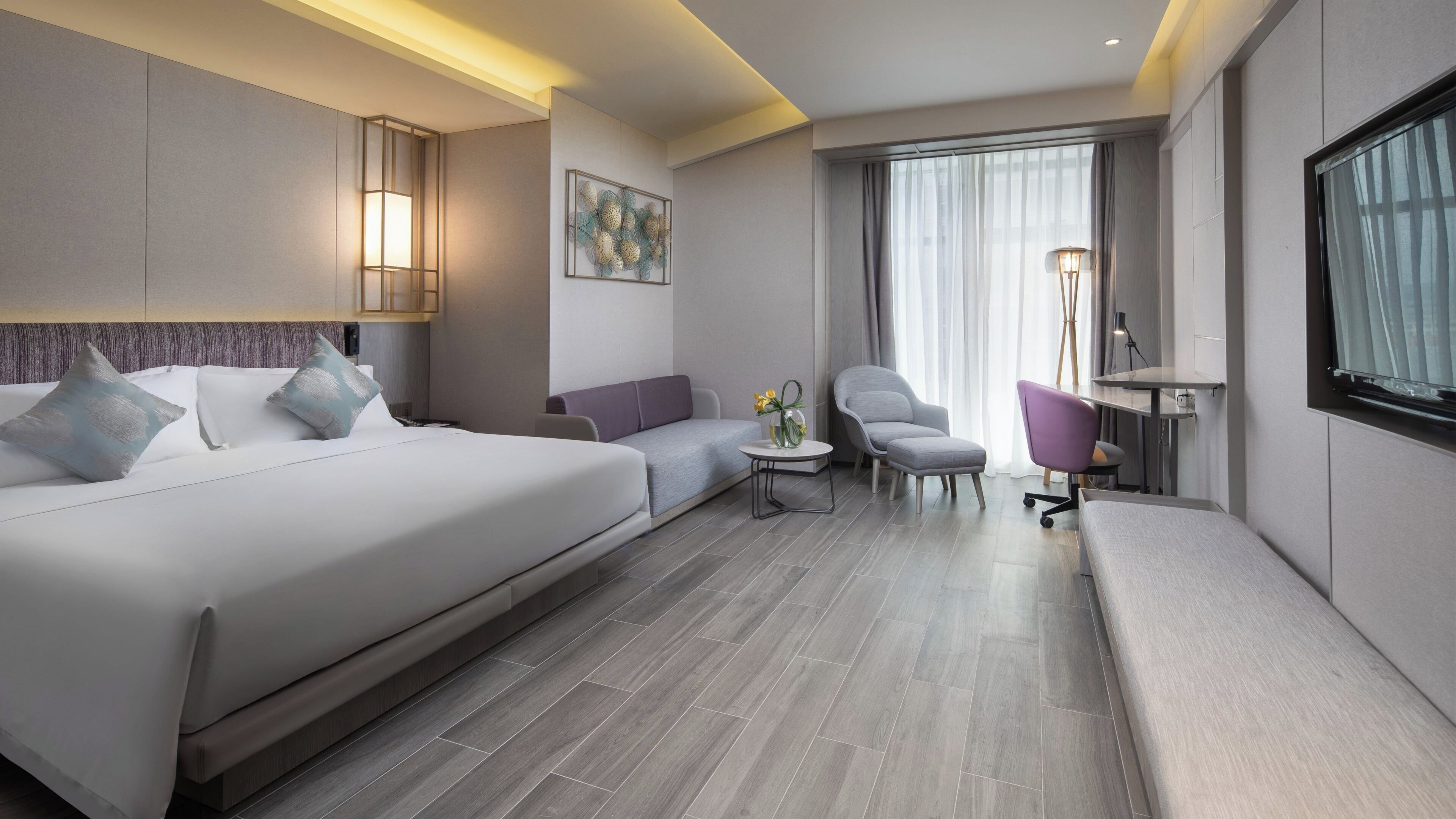 Ein modernes Hotelzimmer mit einem großen Bett, einer Sitzecke, einem kleinen Tisch mit einer Vase, einem Sessel und einem Schreibtisch.