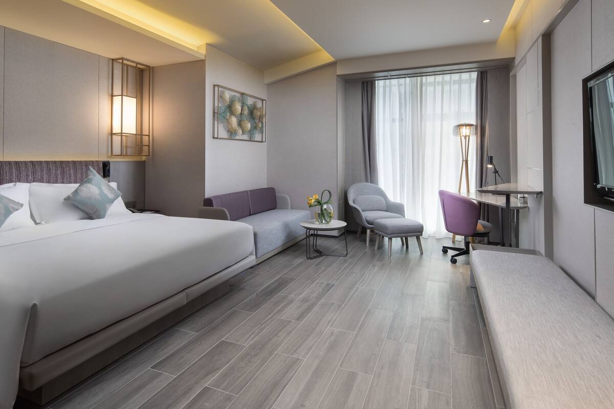 Una habitación de hotel moderna con una cama grande, un sofá, una mesita con un florero, una silla y un escritorio.
