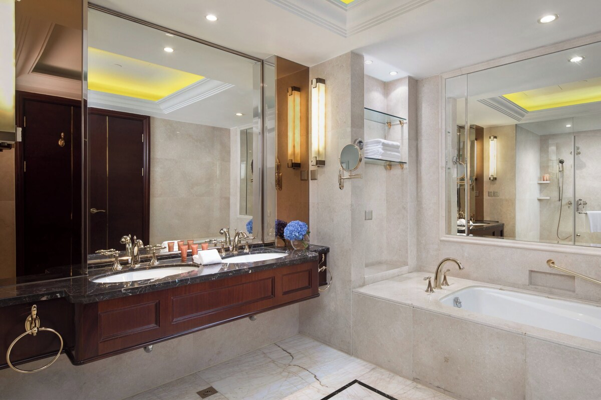 A modern bathroom with a double sink vanity, a large mirror, a bathtub, and a glass shower enclosure.