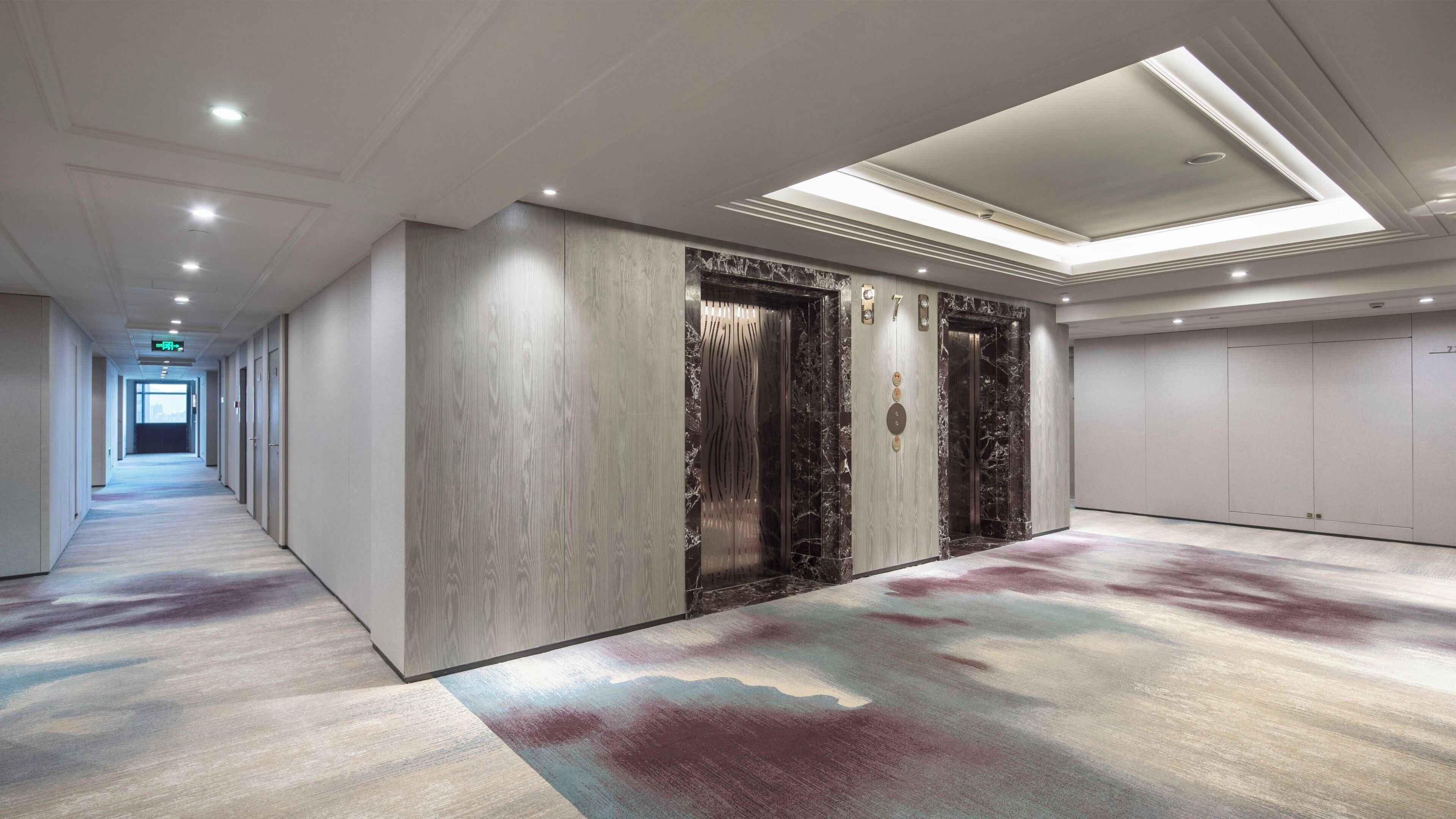 Un pasillo de hotel con piso alfombrado, pared de madera y un ascensor con detalles de mármol.