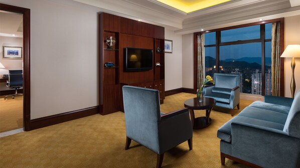 A hotel room with a large window offering a city view, a flat-screen TV mounted on a wooden cabinet, a blue armchair, a round coffee table, and a small side table with a vase of flowers. - Crowne Plaza Deqing Moganshan by IHG (Huzhou)