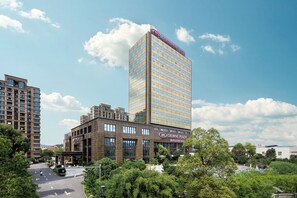 A modern hotel with a prominent glass facade, a rooftop terrace, and a well-maintained surrounding garden. - Crowne Plaza Deqing Moganshan by IHG (Huzhou)