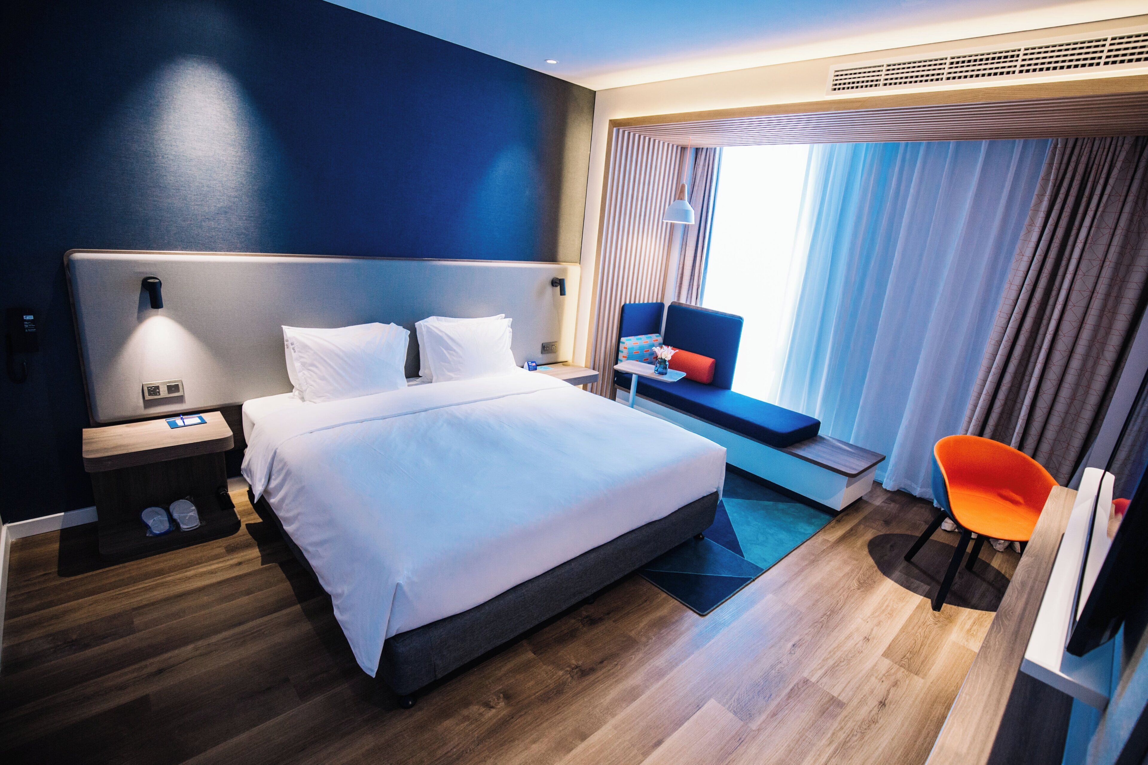 Moderni hotellihuone, jossa on suuri sänky, yöpöydät, työpöytä, tuoli ja ikkuna, jossa on verhot.