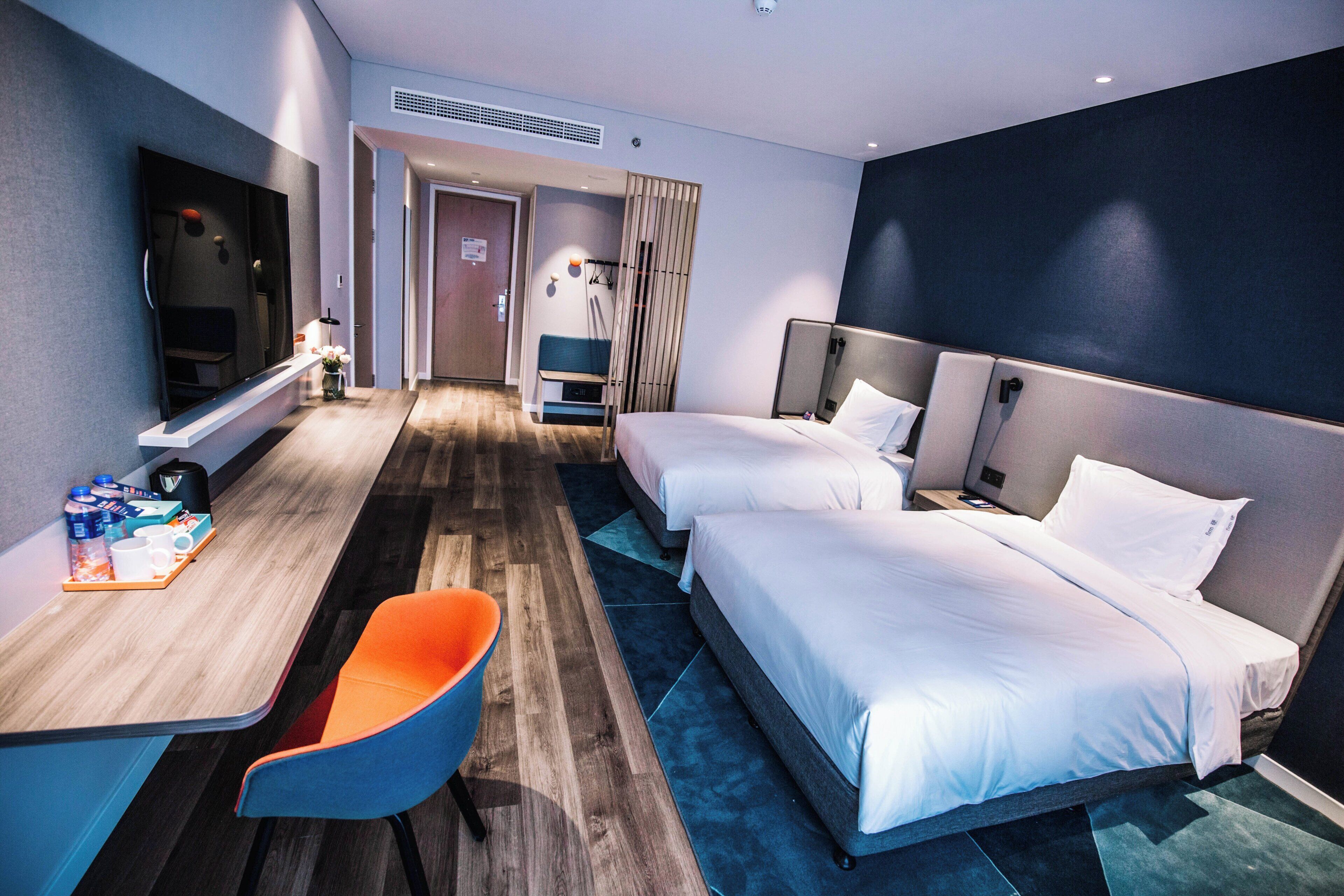 Habitación de hotel con dos camas, un escritorio con silla, televisor y puerta del baño.