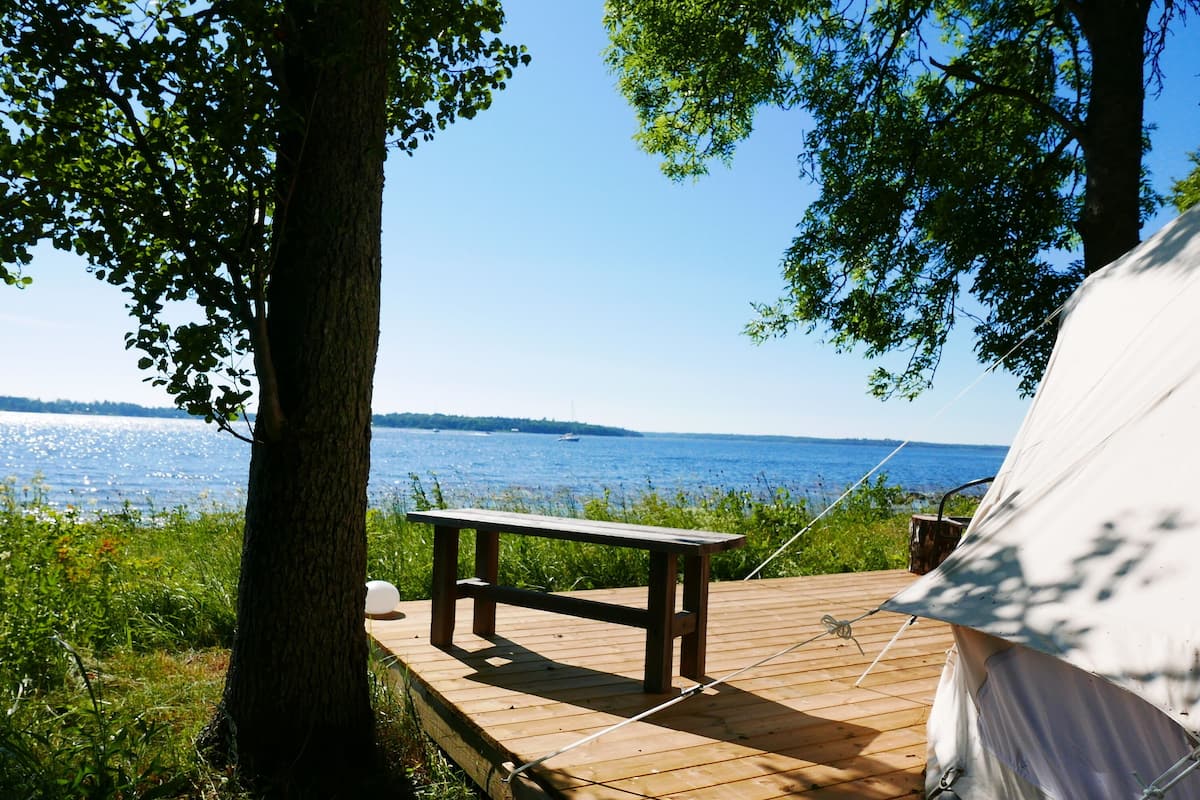 A wooden deck with a table and a tent by a lake.