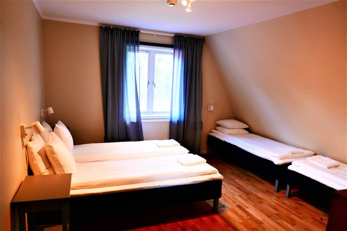 A bedroom with a large bed, two smaller beds, a desk, and a window with curtains.