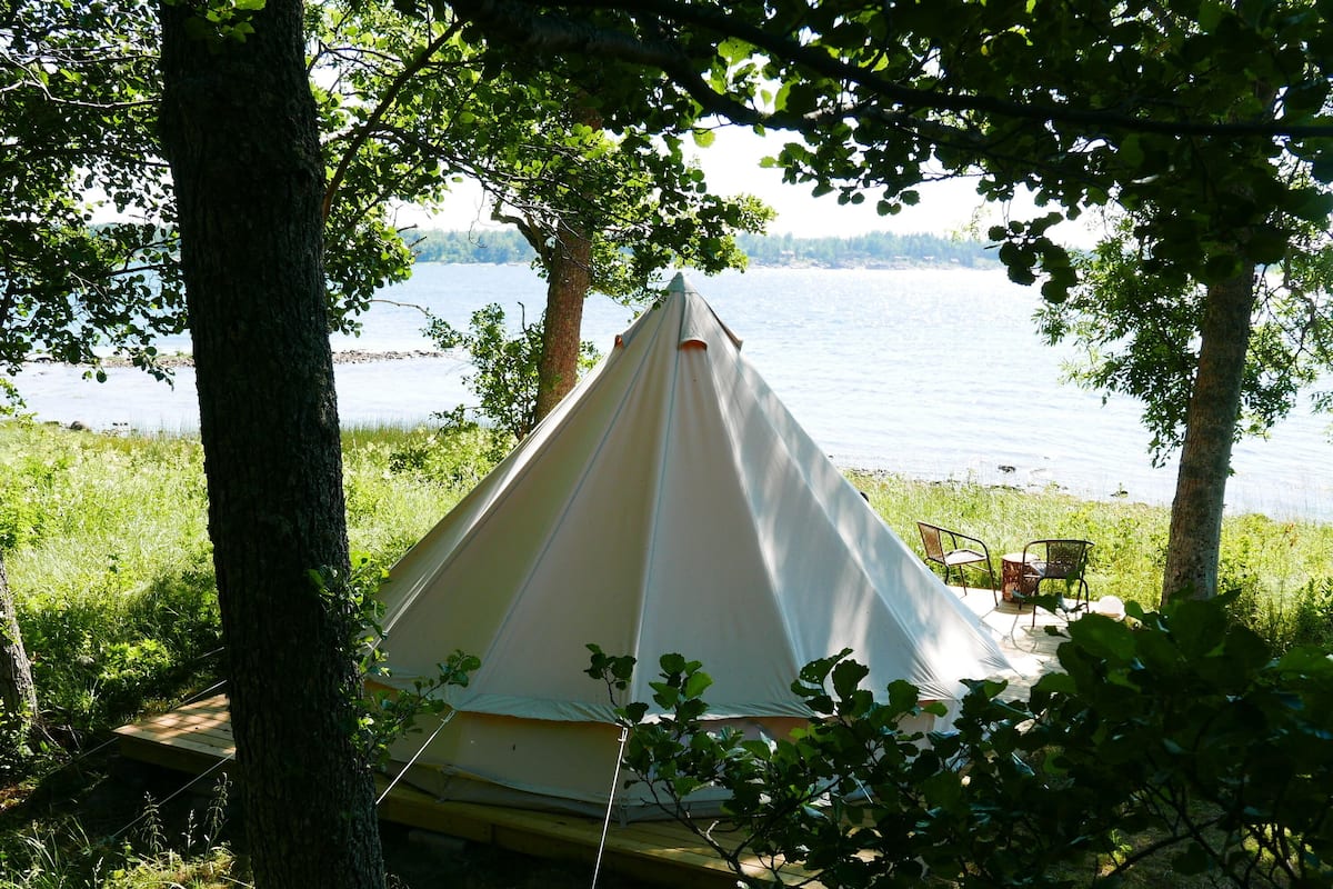 A tent set up by a lake with a chair and table nearby.