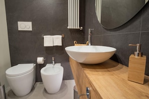 Une salle de bain moderne avec un grand lavabo blanc, deux toilettes, un porte-serviettes et un miroir.