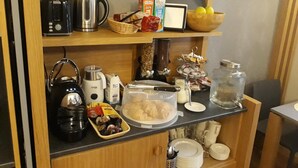 Un plan de travail de cuisine avec divers appareils et aliments, notamment une bouilloire, un grille-pain, une machine à café et un récipient contenant des pâtisseries.