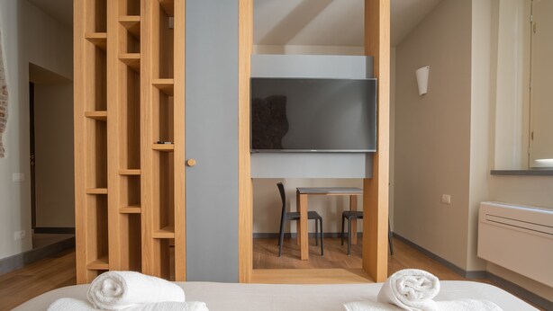 Une chambre d’hôtel avec un lit, deux serviettes, une armoire en bois, une télévision et une petite table avec des chaises.