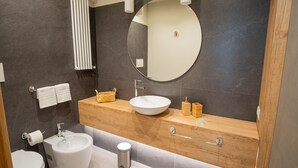Une salle de bain moderne avec un grand miroir rond, un lavabo blanc, un bidet et un porte-serviettes.