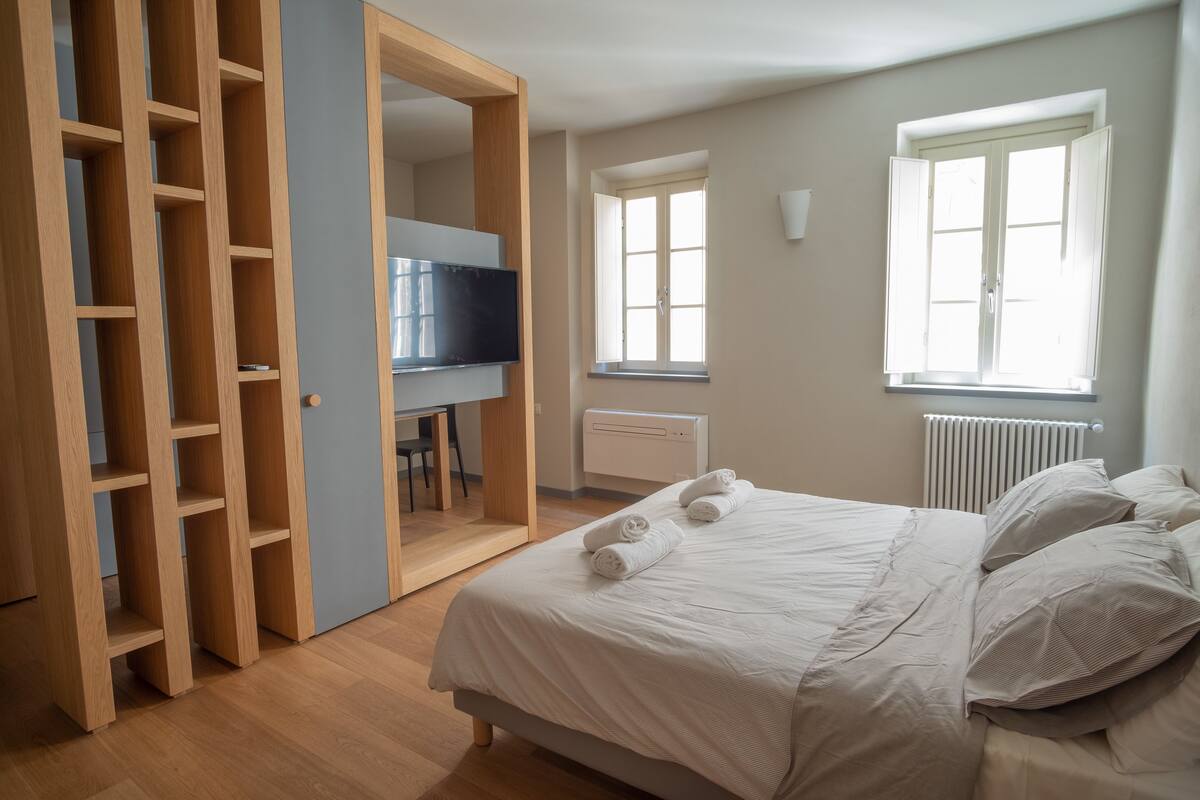 A bedroom with a bed, a wardrobe, a desk, and a television.