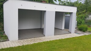 A modern, white, covered outdoor area with a tiled floor and a pathway leading to a door. - VIP Apartmány Žabník (Prievidza)