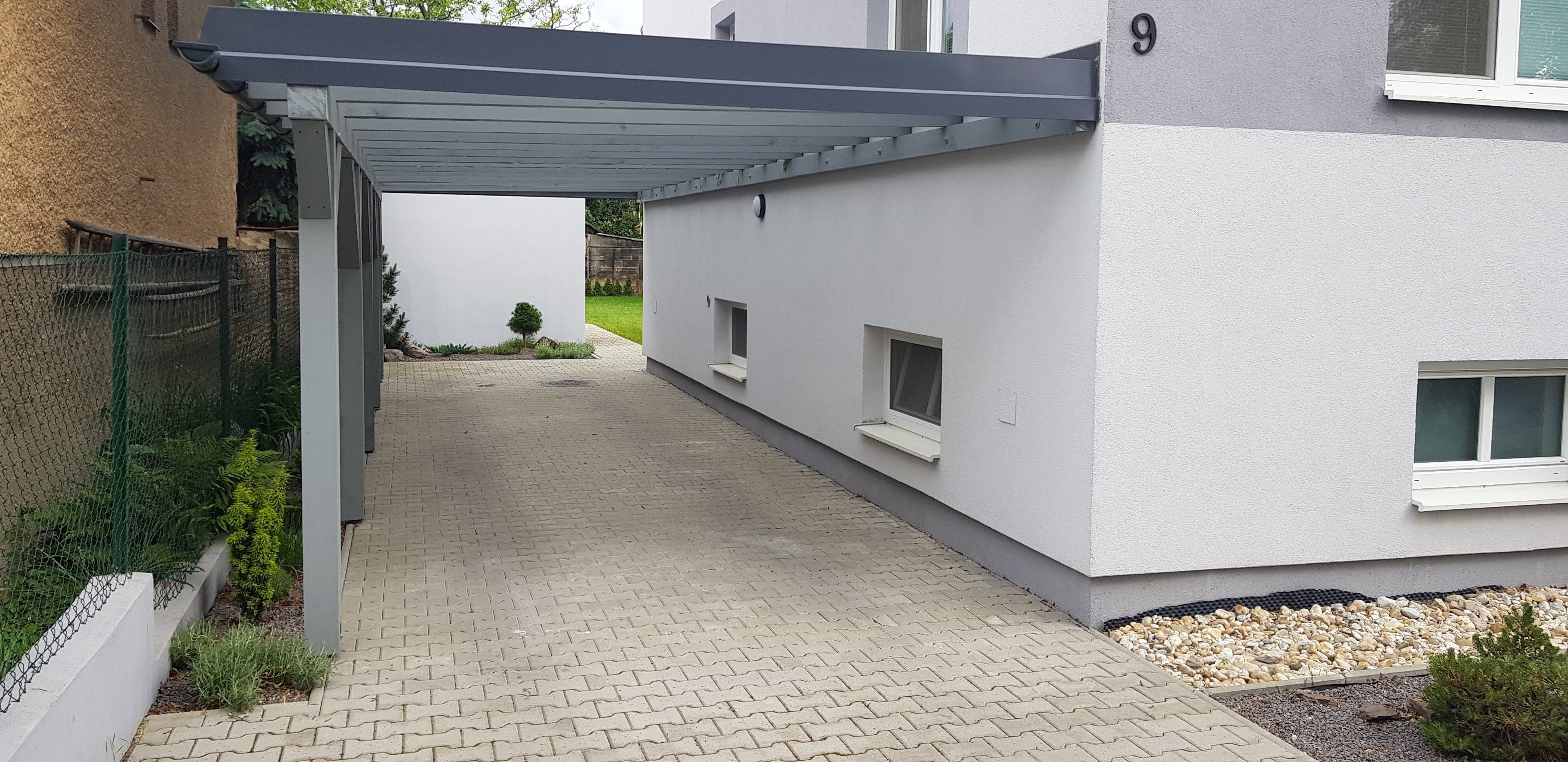 A modern building with a covered walkway, a number '9' on the wall, and a small garden area.
