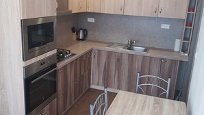 A modern kitchen with wooden cabinets, a built-in oven, a microwave, and a sink. - VIP Apartmány Žabník (Prievidza)
