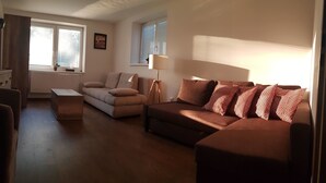 A living room with a brown sofa, a beige sofa, and a wooden coffee table. There is a floor lamp and a window with blinds. - VIP Apartmány Žabník (Prievidza)