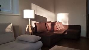 A living room with a sofa, a lamp, and a window with blinds. - VIP Apartmány Žabník (Prievidza)