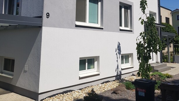 A modern two-story building with a grey facade, multiple windows, and a small garden area with a potted plant. - VIP Apartmány Žabník (Prievidza)