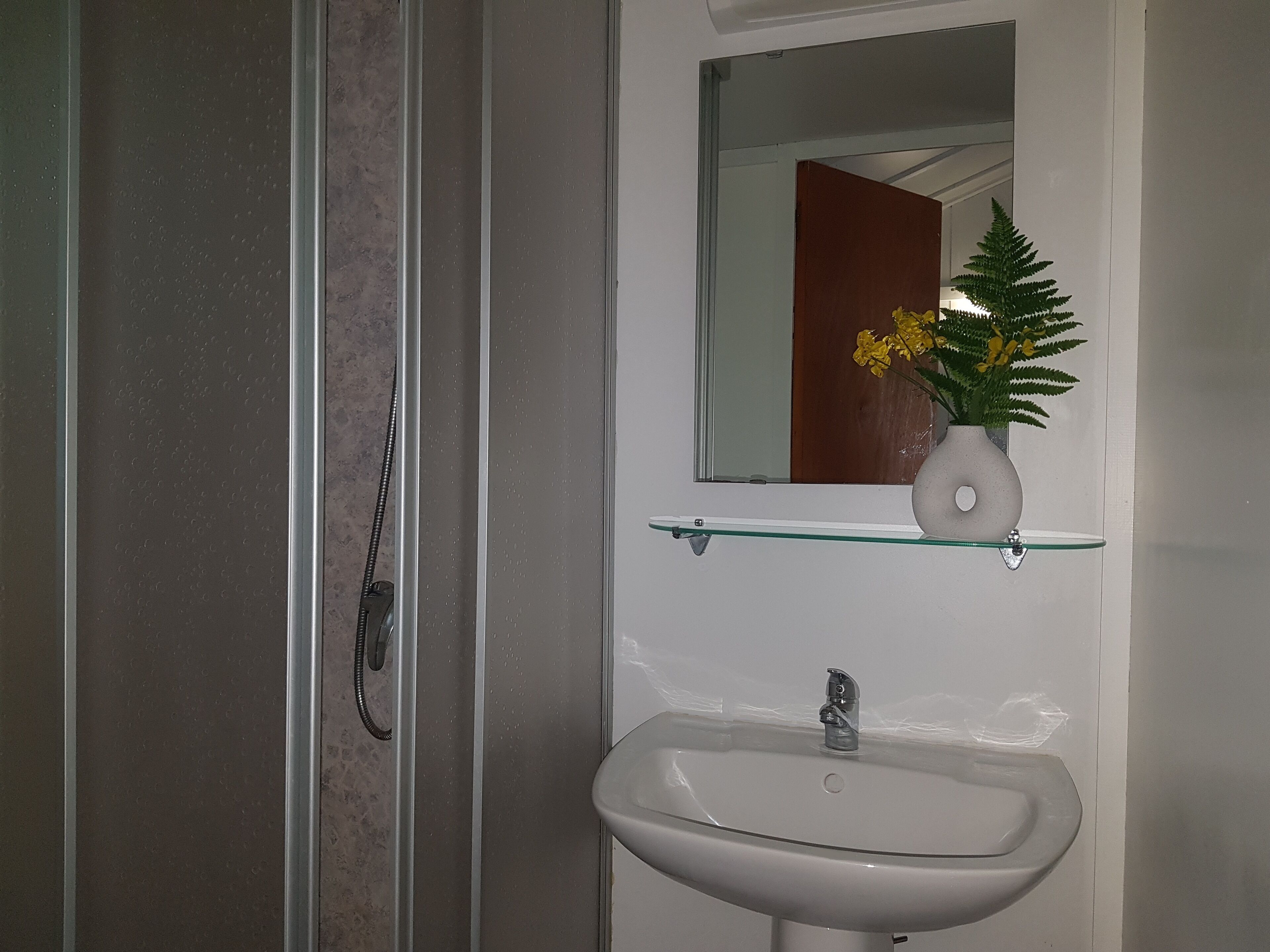 Ein Badezimmer mit einer Duschkabine aus Glas, einem weißen Waschbecken und einem Spiegel darüber.