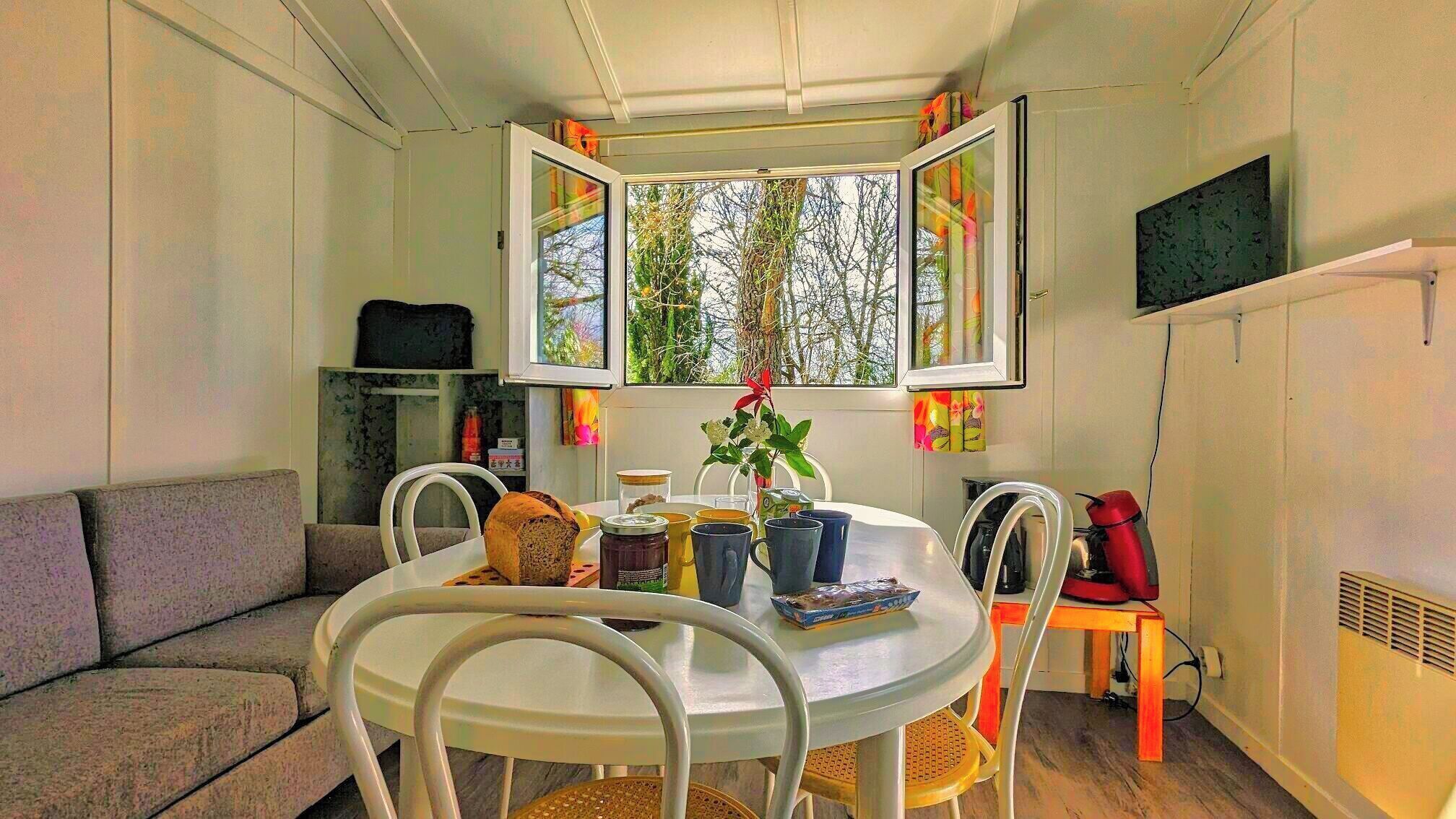 A cozy dining area with a round table, white chairs, and a window with a view of trees.
