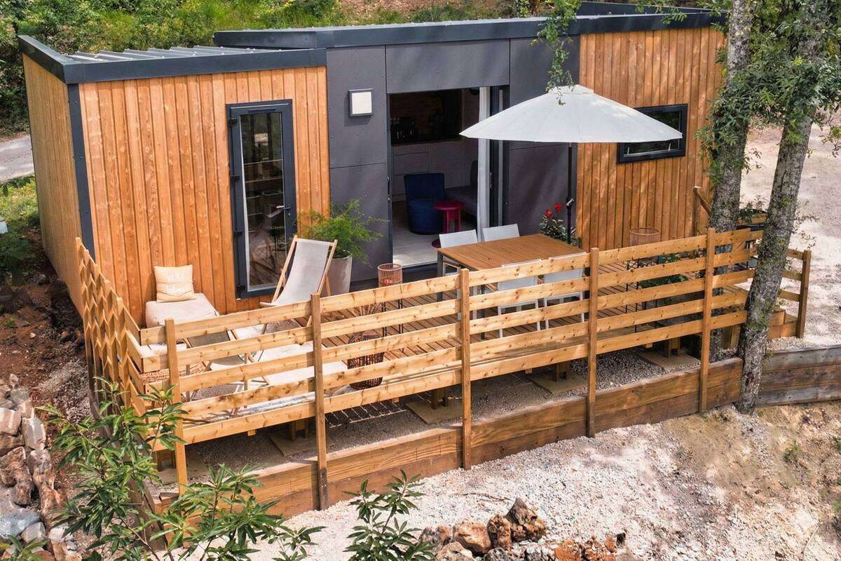 Een moderne houten hut met een terras, een eethoek en een klein zitje buiten.