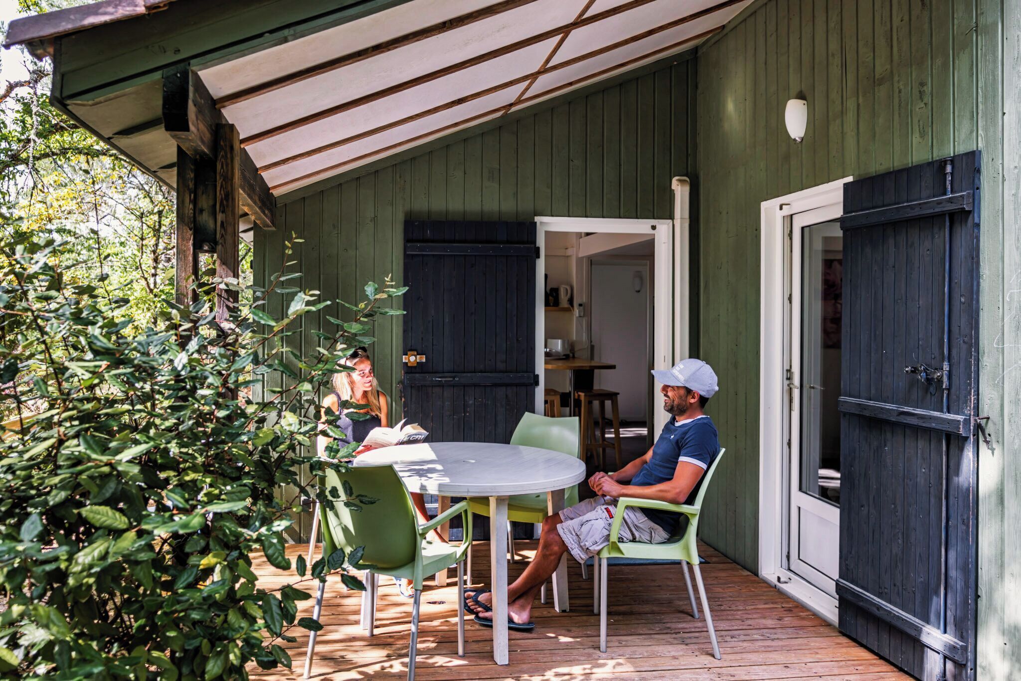 A covered outdoor patio with a round table and chairs, a wooden deck, and a green wall.