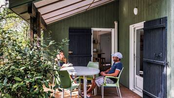 A covered outdoor patio with a round table and chairs, a wooden deck, and a green wall.
