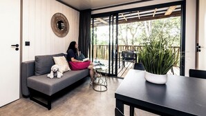 Un salon moderne avec un canapé gris, un miroir rond et un coin repas comprenant une table et des chaises.
